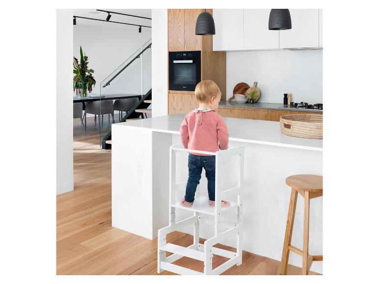 Ein Kind steht auf einem weißen Lernturm neben einer modernen Kücheninsel.