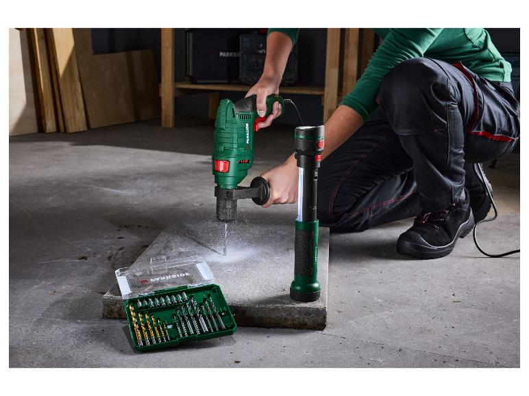 Eine Person benutzt eine Parkside Bohrmaschine, um in eine Betonplatte zu bohren, daneben liegt ein Bohrerset.