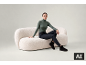 Eine Frau im grünen Rollkragenpullover, dunklen Jeans und schwarzen Stiefeln sitzt auf einem weißen Bouclé-Sofa.