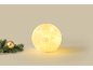 Leuchtende kugelförmige Weihnachtslampe mit Schneeflockenmuster neben Tannenzweig und goldener Kugel