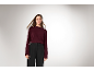 Eine Frau in einem bordeauxroten Strickpullover und einer schwarzen Hose.