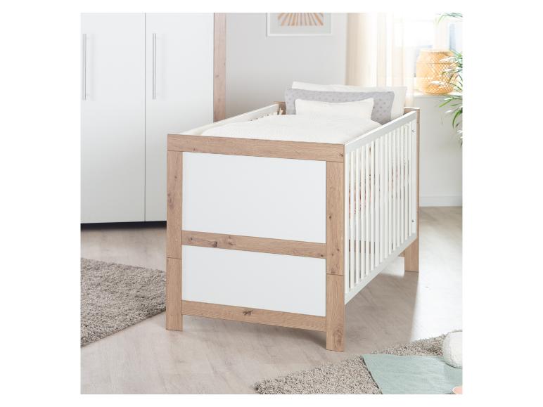 Weißes und hölzernes Babybett mit Bettwäsche in einem hellen Kinderzimmer.