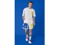 Mann in weißem T-Shirt, weißen Shorts mit farbigen Taschen und Turnschuhen.