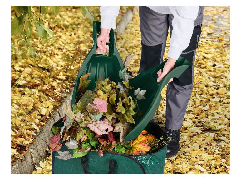 Person schaufelt Herbstlaub mit Laubgreifern in einen grünen Gartenabfallsack.
