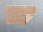 Beige Badezimmermatte mit Textur auf einem grauen Fliesenboden.