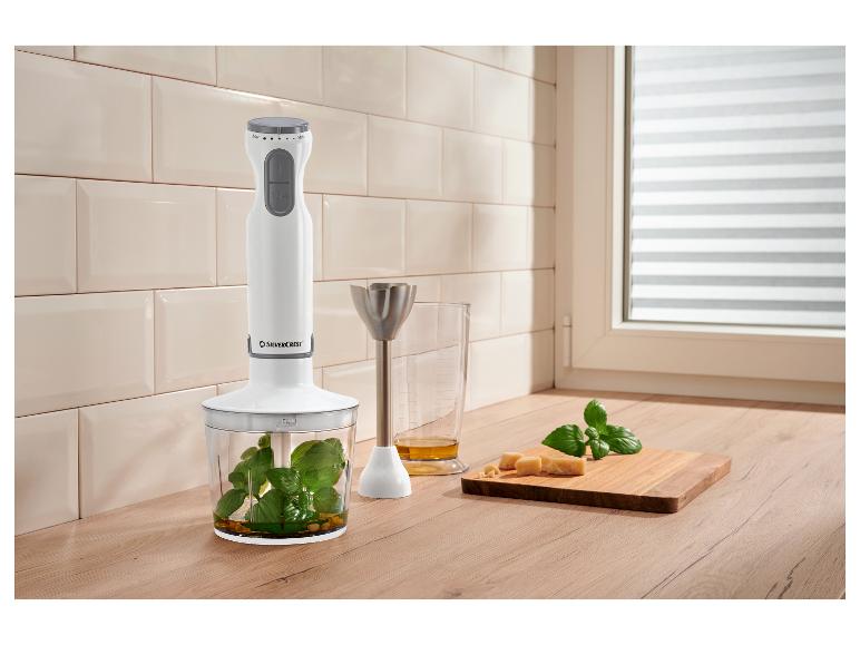 Stabmixer mit Zerkleinereraufsatz, Messbecher mit Öl, Käse und Basilikum auf Holzbrett.