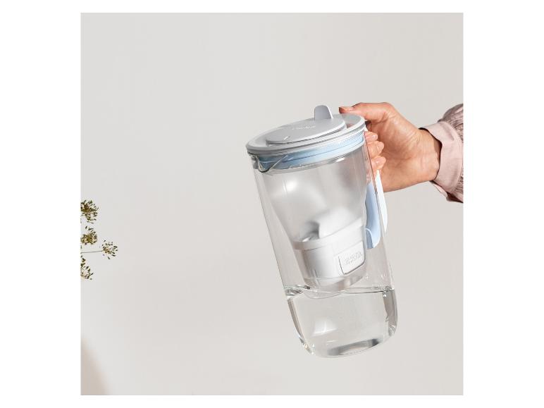 Eine Hand hält einen transparenten Wasserfilterkrug mit Wasser am Boden.