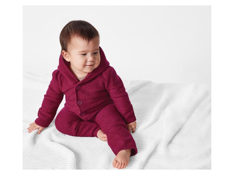 Ein Baby in einem dunkelroten Fleece-Strampler mit Kapuze.