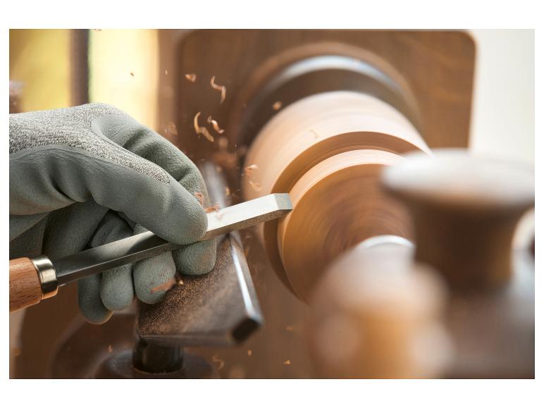 Eine handbeschützte Hand verwendet einen Meißel, um eine Holzscheibe auf einer Drehbank zu bearbeiten.