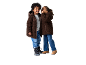 Zwei Kinder in braunen Teddyfleecejacken und Jeans, eines flüstert dem anderen zu.