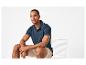 Mann in marineblauem Poloshirt und beigefarbenen Shorts sitzt auf einem weißen Stuhl.
