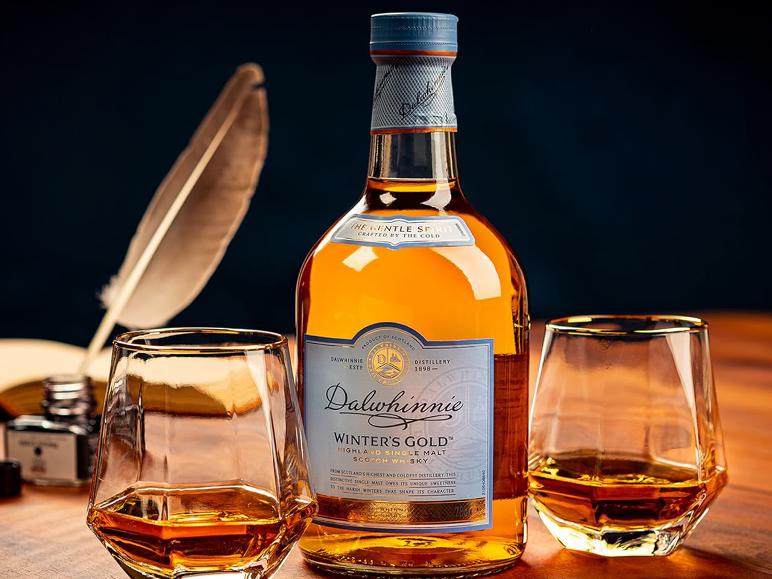 Flasche 'Winter's Gold' Whisky mit zwei Gläsern, Feder und Tinte auf Holzoberfläche.