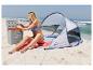Frau am Strand sitzt neben Zelt und Kühlbox, öffnet eine Flasche.