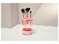 Rosa Make-up-Pinselreiniger mit vier Pinseln, auf einer weißen Oberfläche mit hellem Hintergrund.