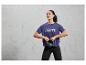 Eine Frau in einem blauen Sport-Shirt mit dem Aufdruck 'Break the Limits' hält eine schwarze Kettlebell.