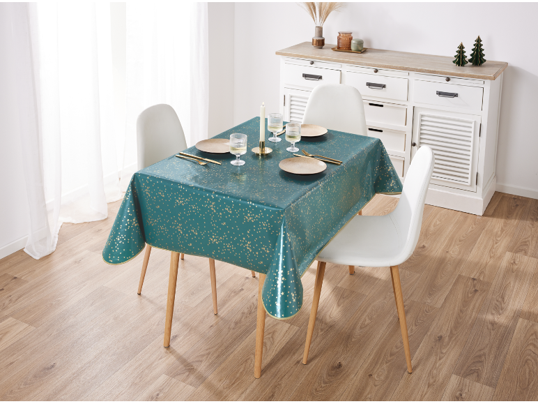 Esstisch mit einer tealfarbenen Tischdecke mit goldenen Sternen, gedeckt mit Tellern, Gläsern und Besteck.