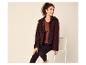 Frau in brauner Teddyfleecejacke, braunem Top und schwarzen Leggings, auf einem Stuhl sitzend.