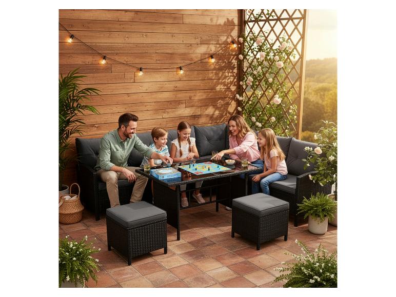 Familie spielt Brettspiel auf Rattan-Gartenmöbeln auf einer Holzterrasse.