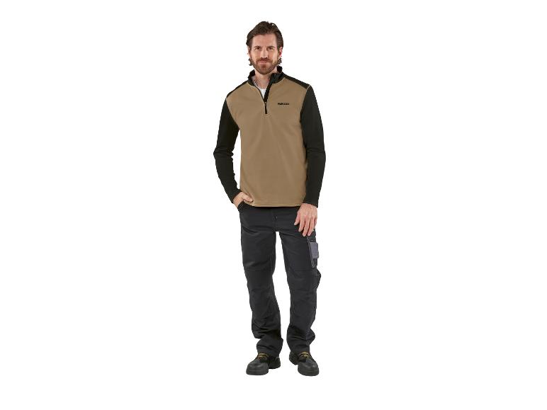 Mann trägt einen beigefarbenen und schwarzen Parkside-Pullover und schwarze Arbeitshosen.
