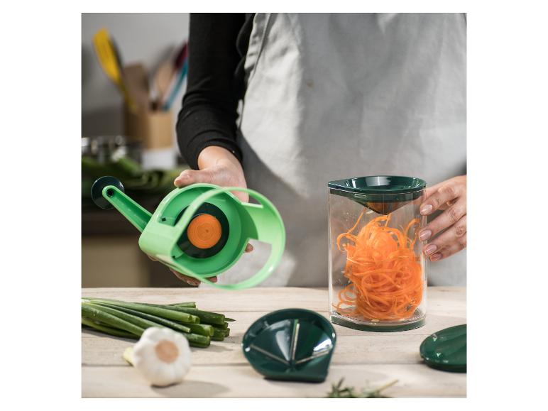 Person benutzt einen Spiralschneider, um Karottennudeln zuzubereiten, mit Knoblauch und Lauchzwiebeln auf dem Tisch.