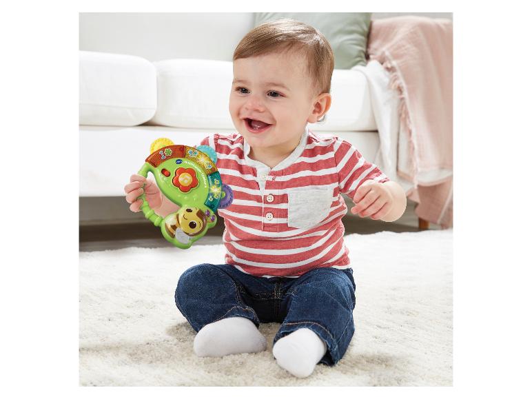 Glückliches Baby spielt mit einem bunten Bienen-Tamburin auf einem weißen Teppich.