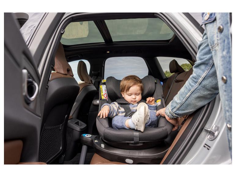Ein Baby sitzt in einem drehbaren Autositz auf dem Rücksitz eines Autos.
