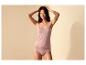 Frau in einem rosa Camisole mit Spitze und passendem Slip, Hände im Haar, lächelnd.