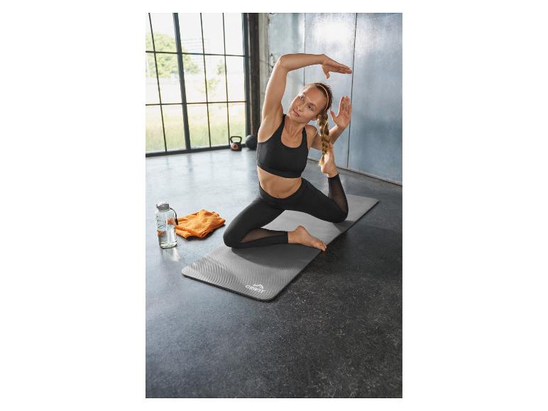 Frau macht Yoga auf einer Matte, mit Wasserflasche und Handtuch daneben.