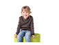 Lächelndes Kind in Pullover und Jeans sitzt auf einem grünen Hocker.
