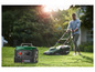 Ein grüner Parkside Generator auf dem Rasen, im Hintergrund ein Mann, der mit einem Rasenmäher mäht.