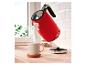 Roter Wasserkocher mit „1973“-Aufschrift gießt Wasser in eine Tasse auf einer Holztheke.