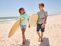 Zwei Kinder laufen am Strand mit Surfbrettern.