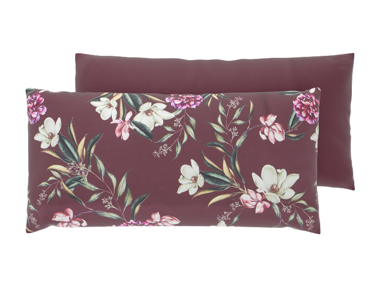 Zwei burgunderrote Kissen, eines mit einem Blumenmuster aus weißen und rosa Magnolien und grünen Blättern.