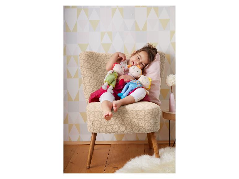 Ein glückliches Kind sitzt auf einem Stuhl mit drei weichen Puppen.