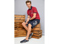 Mann trägt ein rotes Poloshirt, schwarze Shorts mit 'Royal Navy'-Aufdruck und blaue Sandalen.