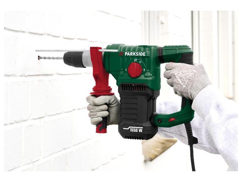 Grüne und schwarze 1550 W Schlagbohrmaschine, die eine weiße Ziegelwand bohrt.