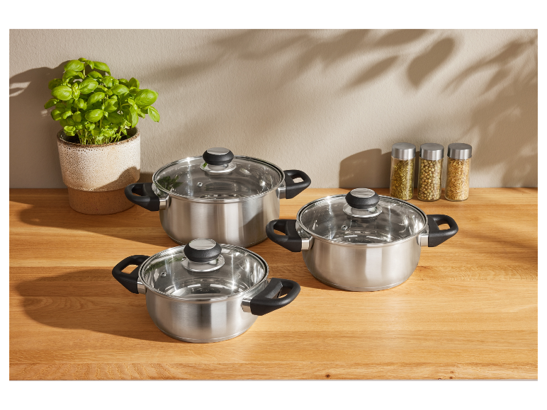 Drei Edelstahl-Töpfe mit Glasdeckeln auf einer Holztheke.