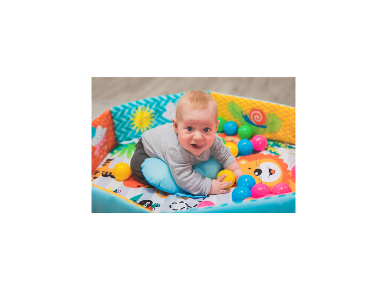 Baby spielt in einem bunten Bällebad mit einem weichen Kissen.