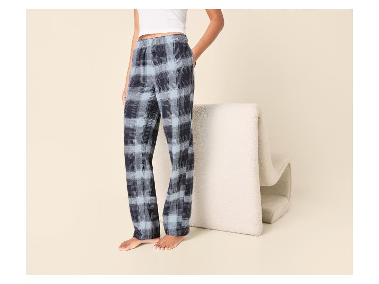 Frau in blau karierter Pyjamahose, stehend neben einem beigen Sessel.