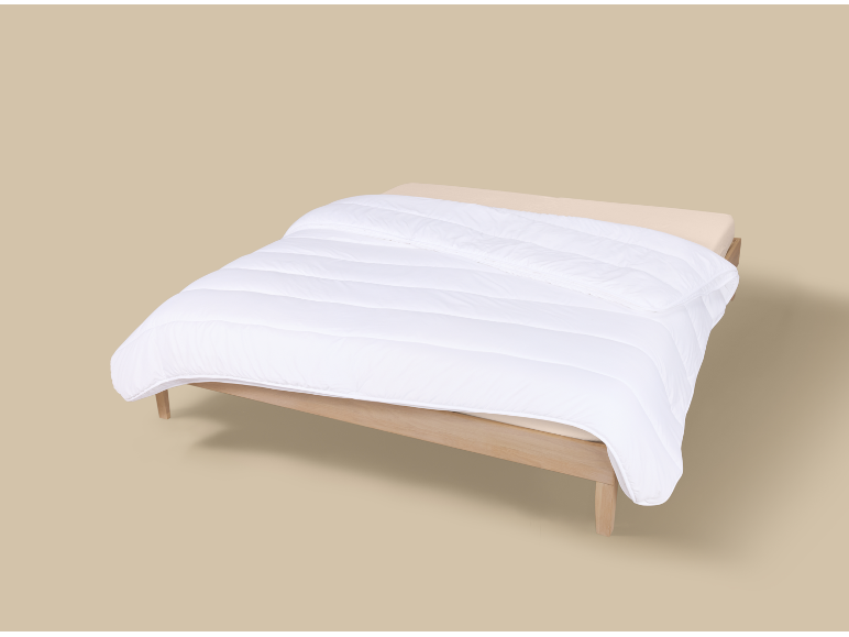 Bett mit weißer Bettdecke und hellem Holzrahmen auf beigem Hintergrund.