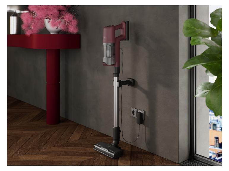 Roter AEG-Stielstaubsauger lädt an grauer Wand neben roter Konsole.