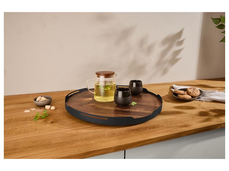Holztablett mit Glasteekanne, schwarzen Tassen, Keksen und Zucker auf einer Holztheke.