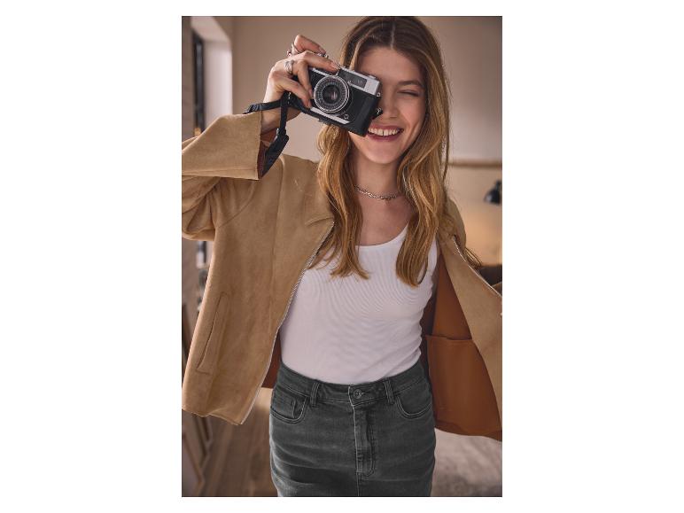 Frau in beige Jacke und Jeansrock, die mit einer alten Kamera ein Foto macht.