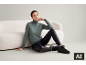 Frau in grünem Rollkragenpullover und schwarzen Leggings sitzt neben einem Sofa.
