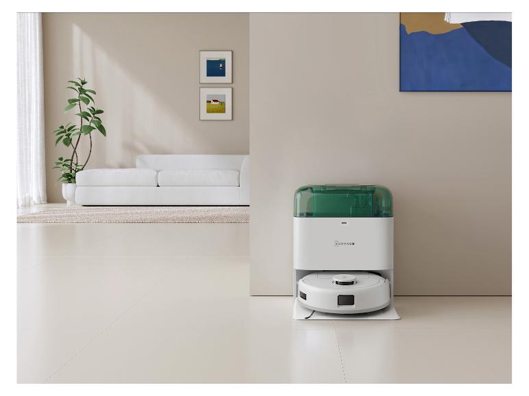 Weißer Saugroboter mit grüner Ladestation in einem modernen Wohnzimmer.