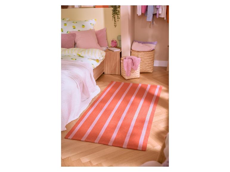 Schlafzimmer mit Zitronen-Bettwäsche, rosa Kissen und einem gestreiften orange-rosa Teppich.
