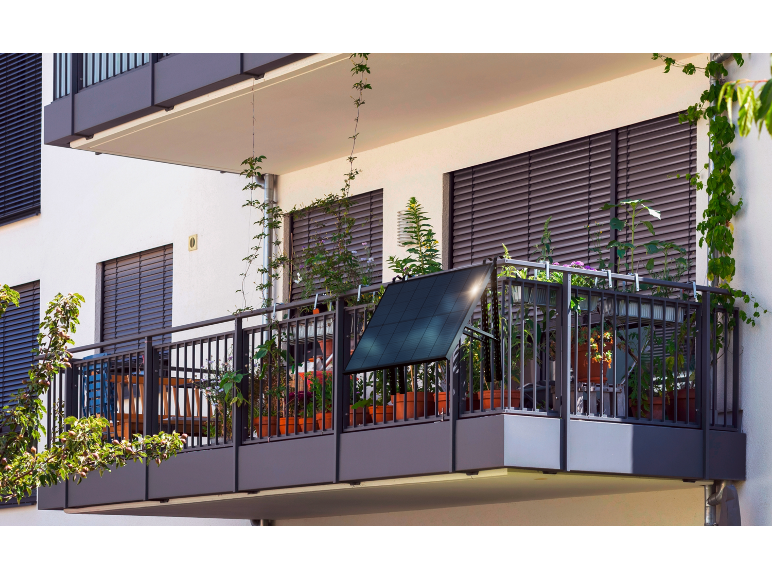 Balkon mit Topfpflanzen und einem Solarpanel am Geländer.