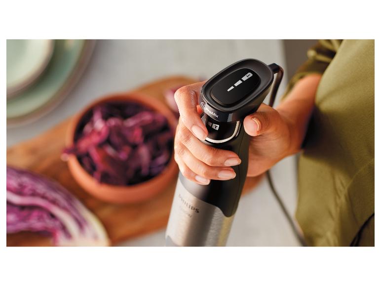 Hand hält einen Stabmixer mit Rotkohl in einer Schüssel im Hintergrund.