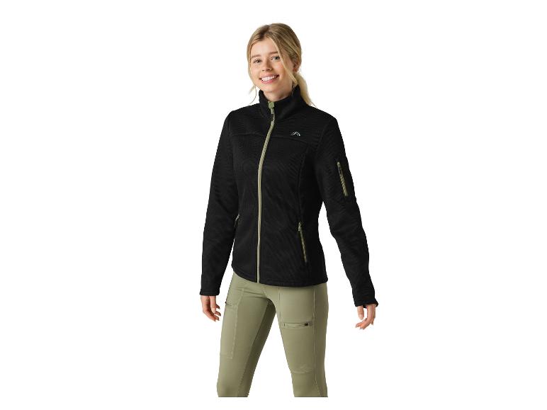 Frau in schwarzer Fleecejacke mit Reißverschluss und olivgrüner Hose, lächelnd.