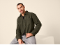 Sitzender Mann in einer dunkelgrünen Fleecejacke und grauen Jeans.
